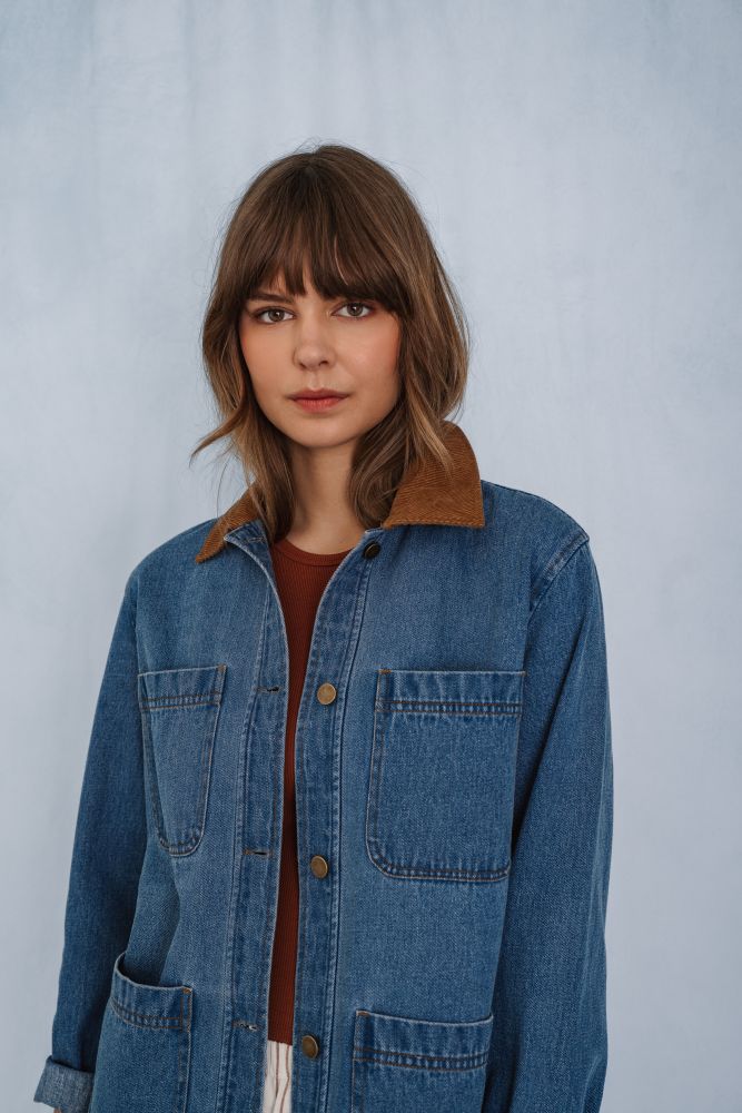 Woman wearing a blue denim barn jacket with a brown collar against a plain background