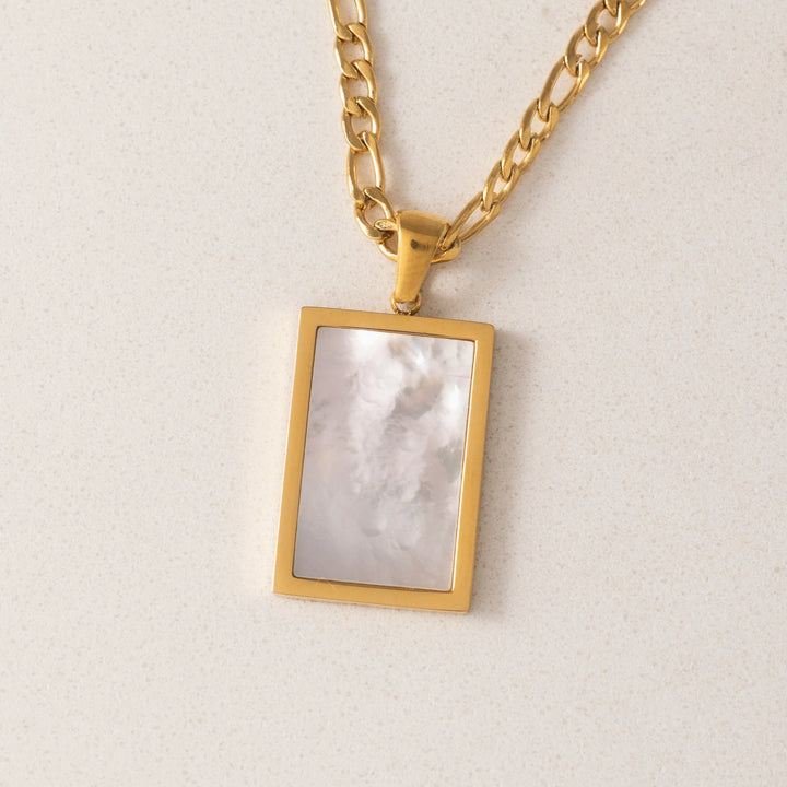 Gold necklace with a rectangular pendant on a light background