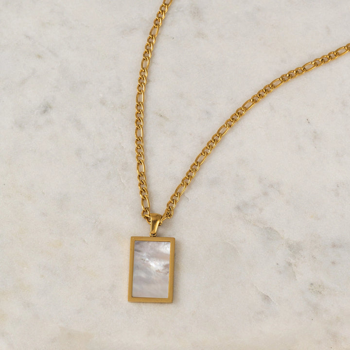 Gold necklace with a rectangular pendant on a marble surface