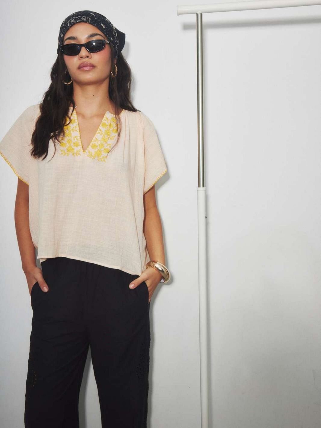 Woman wearing a beige cotton  top with yellow floral embroidery with a retro boho style.