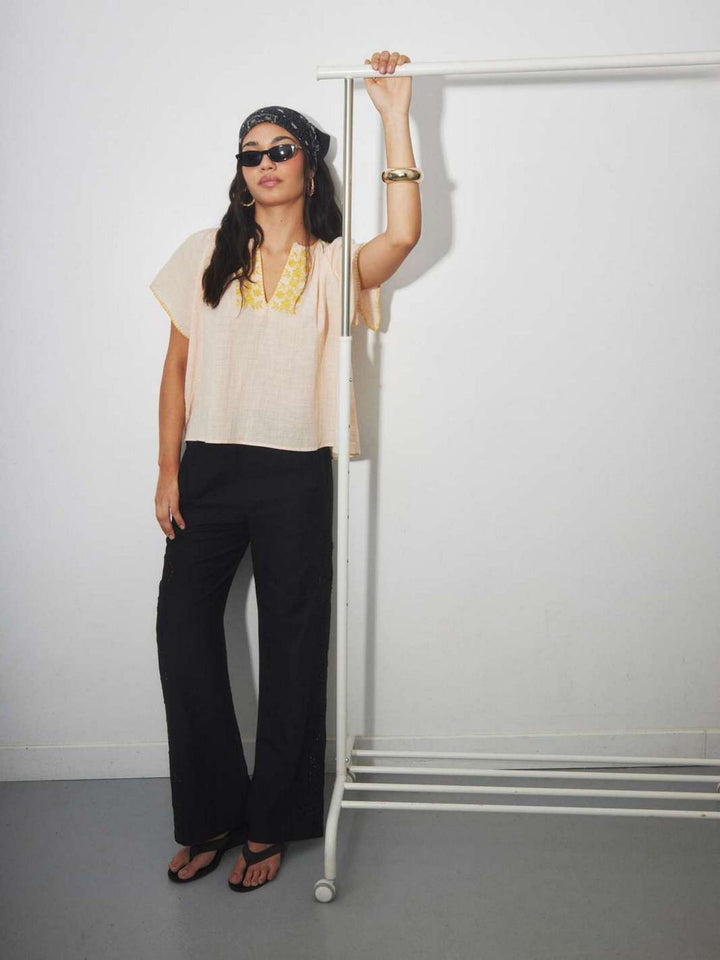 Woman wearing a beige cotton  top with yellow floral embroidery with a retro boho style.