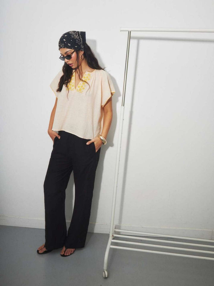 Woman wearing a beige cotton  top with yellow floral embroidery with a retro boho style.