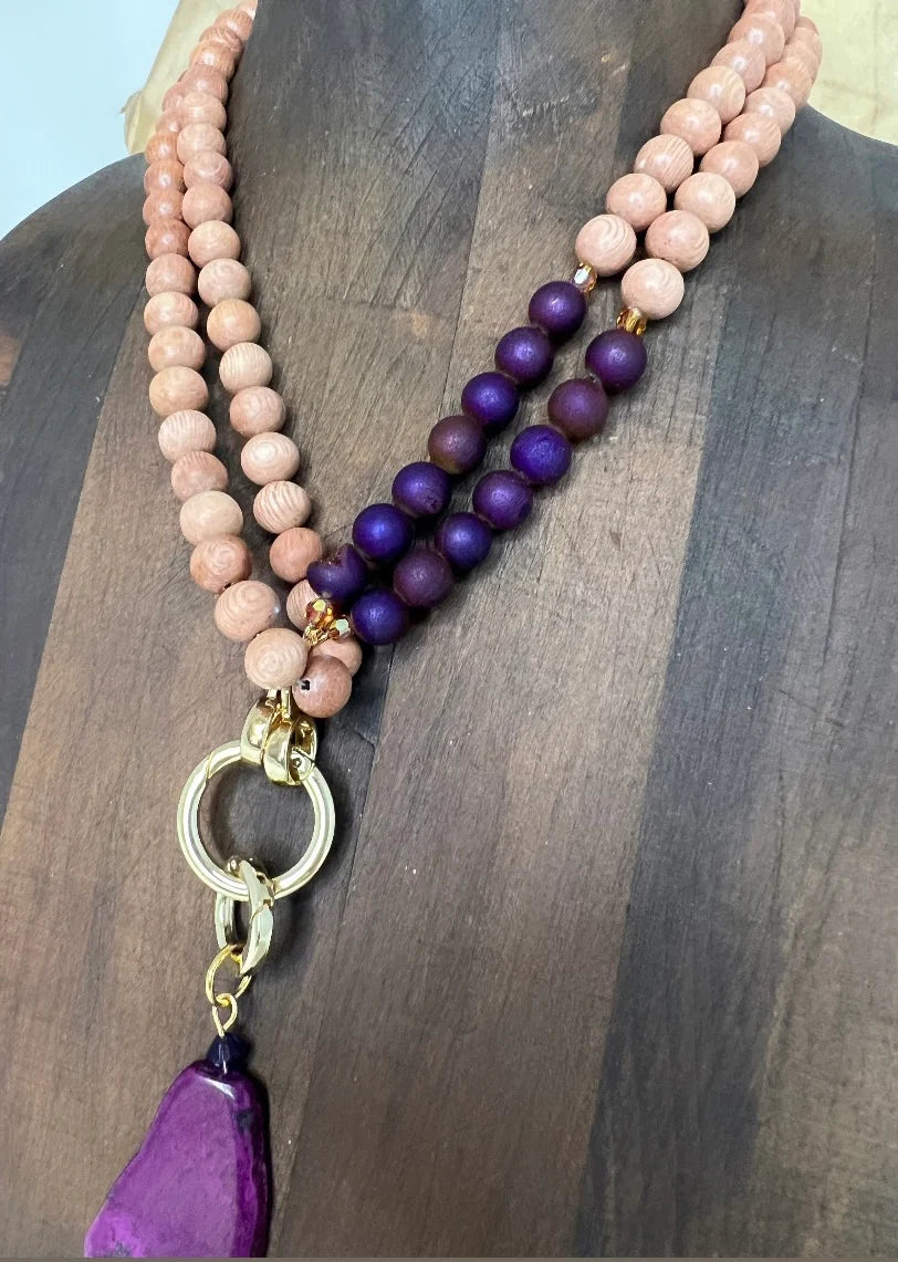 Necklace with rosewood and purple beads and a gold pendant on a wooden surface
