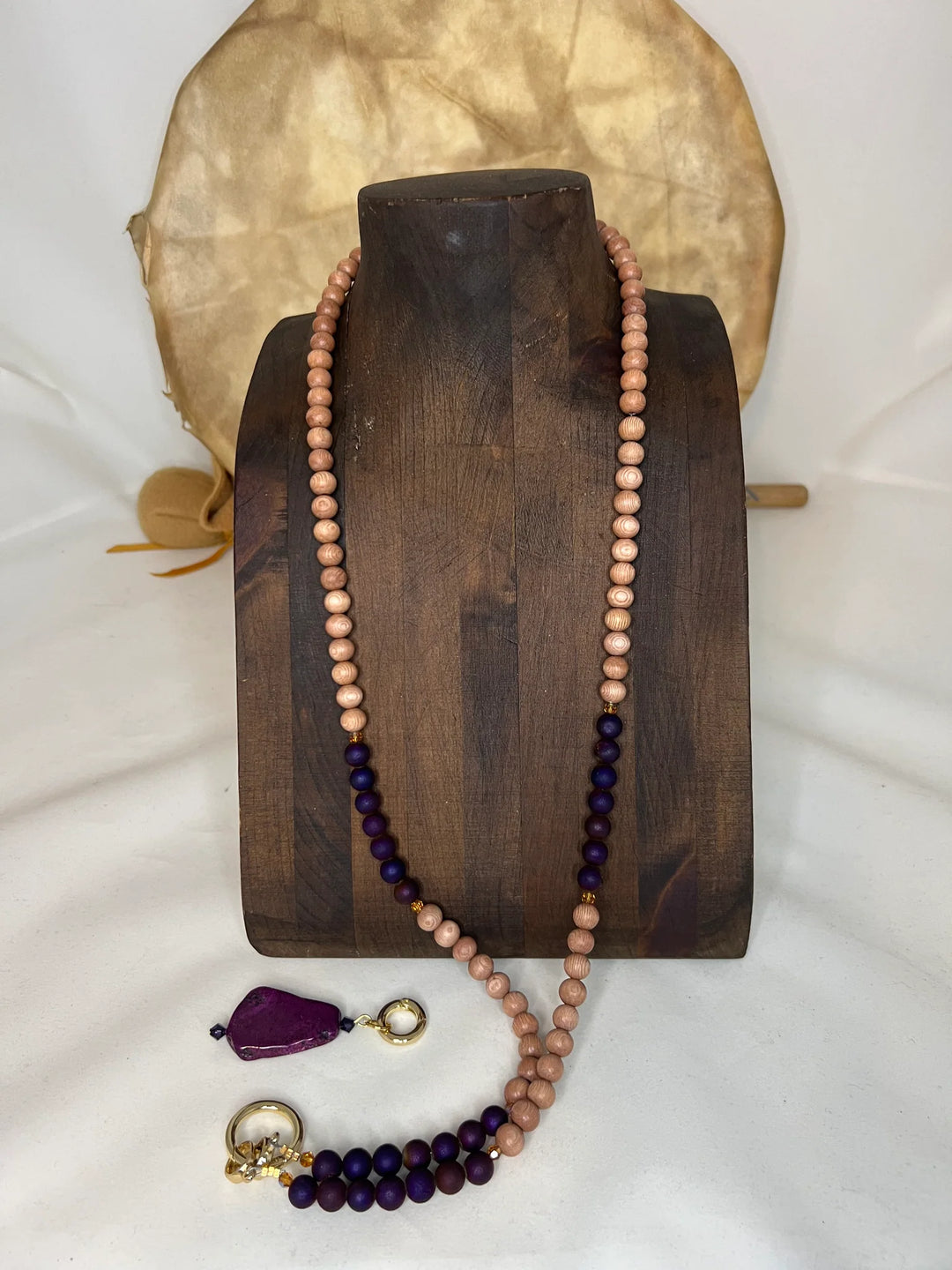 Beaded necklace with purple and rose wood beads on a wooden stand with a white background