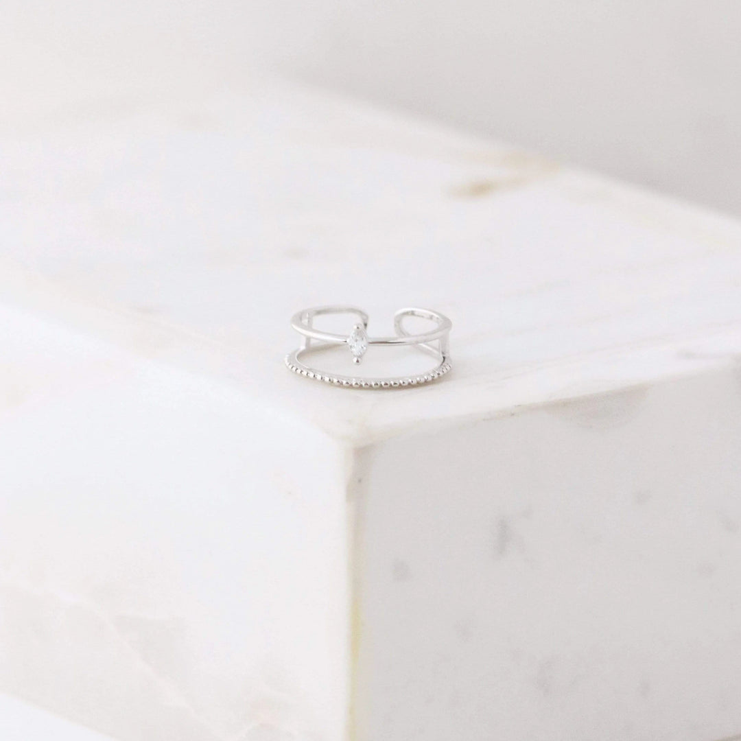 Silver double band ring with a small cubic zirconia diamond  on a white marble surface