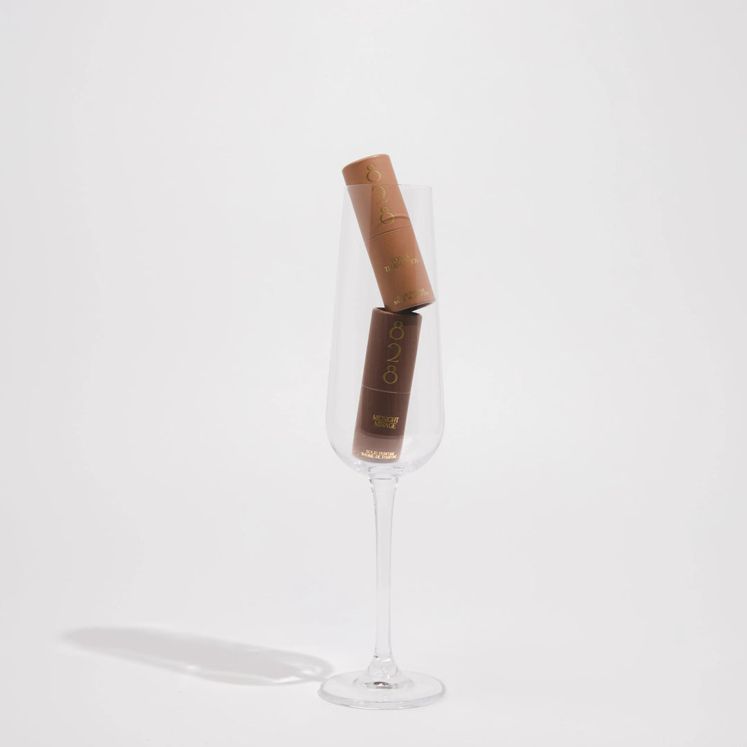 Two solid perfume sticks displayed in a clear glass on a white background