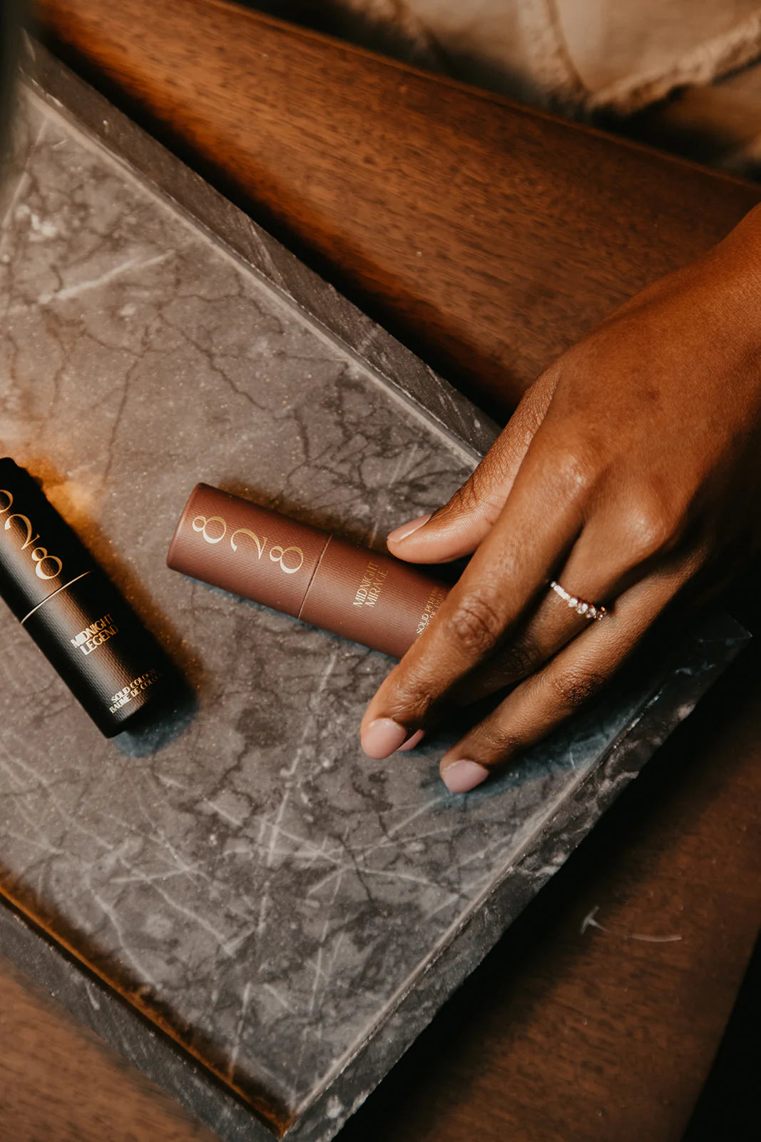 Hand holding a Midnight Mirage solid perfume stick on a marble surface with a blurred background