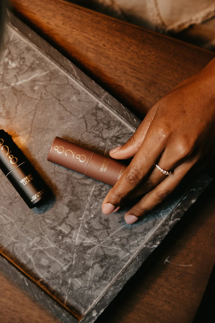 Hand holding a Midnight Mirage solid perfume stick on a marble surface with a blurred background