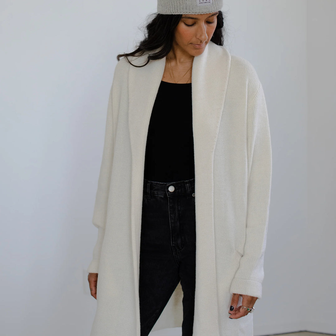 Person wearing a long cream cardigan over a black outfit against a plain background
