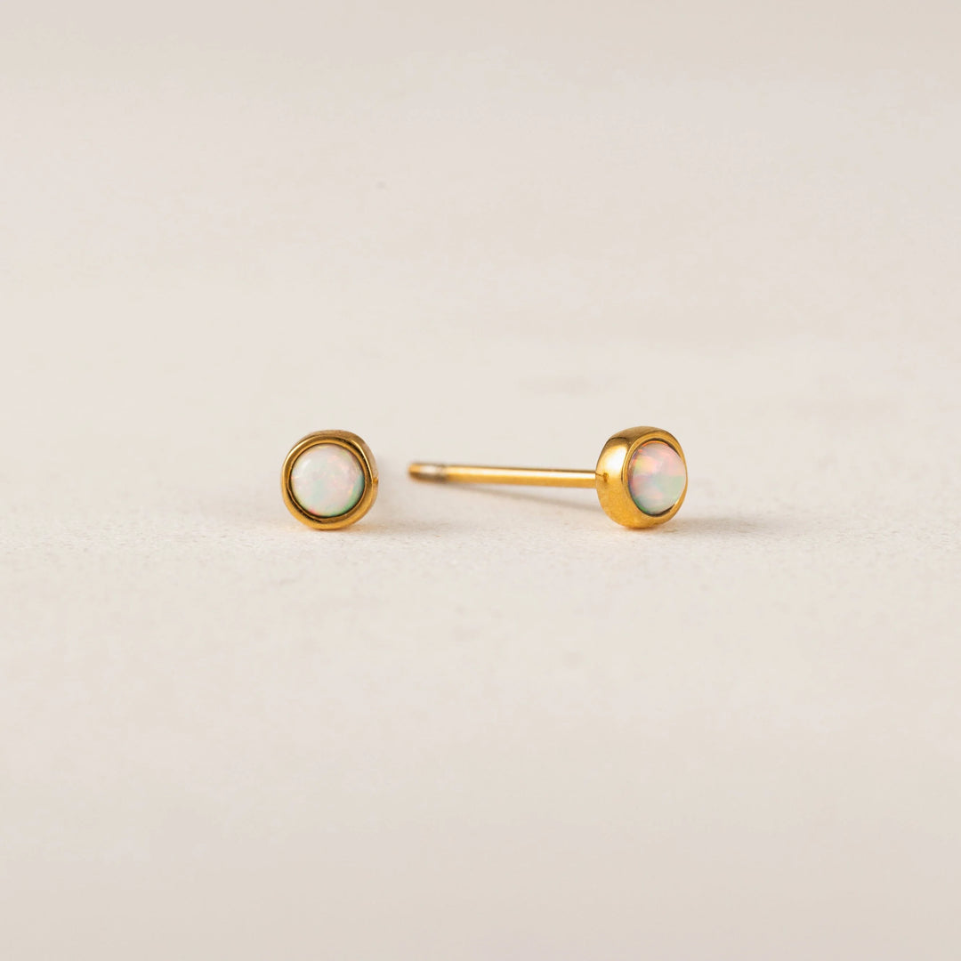 Pair of gold earrings with opal stones on a beige background