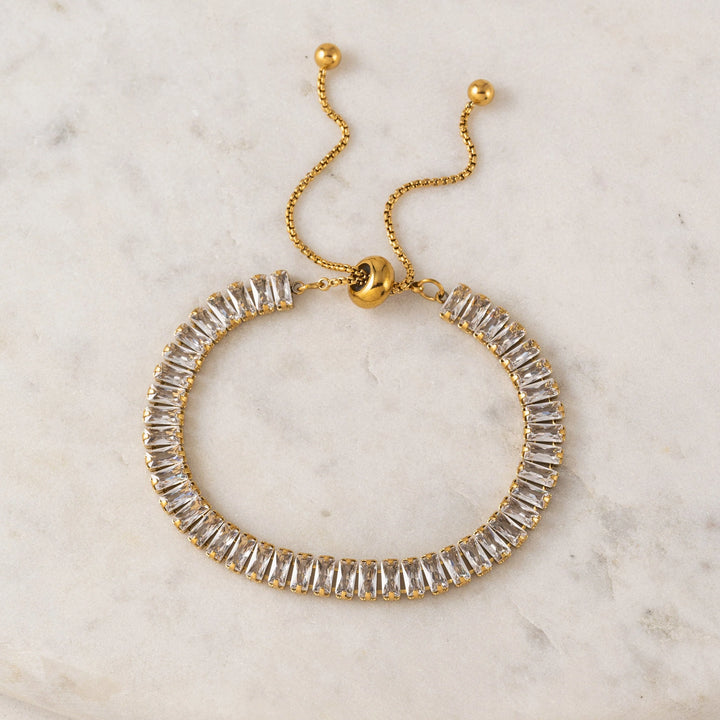 Gold bracelet with clear gemstones on a marble surface
