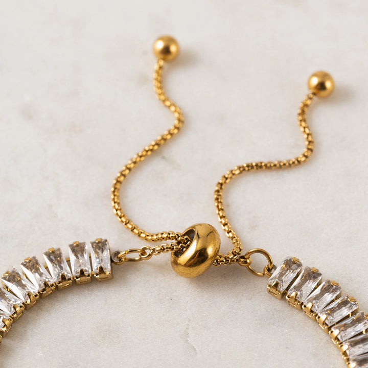 Gold bracelet with clear gemstones on a light marble background