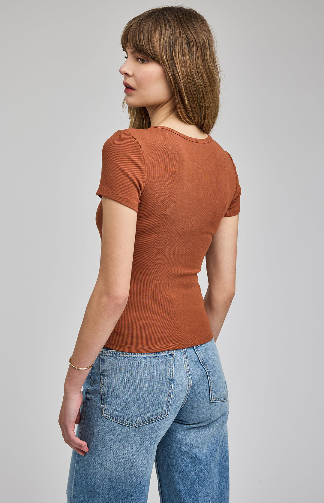 Woman wearing a brown ribbed t-shirt and blue jeans on a gray background