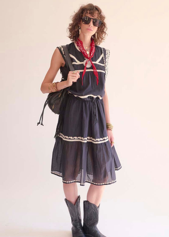 Woman wearing a black dress with white trim, gray boots, and a red scarf, holding a black bag.