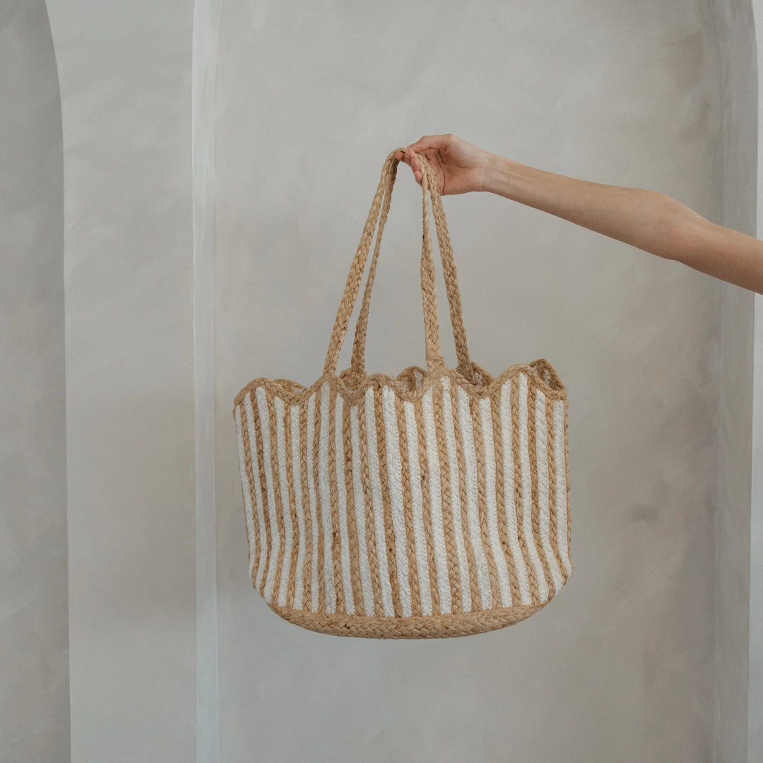 Hand holding a woven bag with striped pattern against a plain background