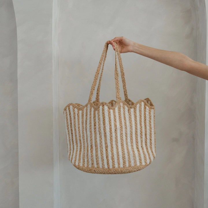 Hand holding a woven bag with striped pattern against a plain background