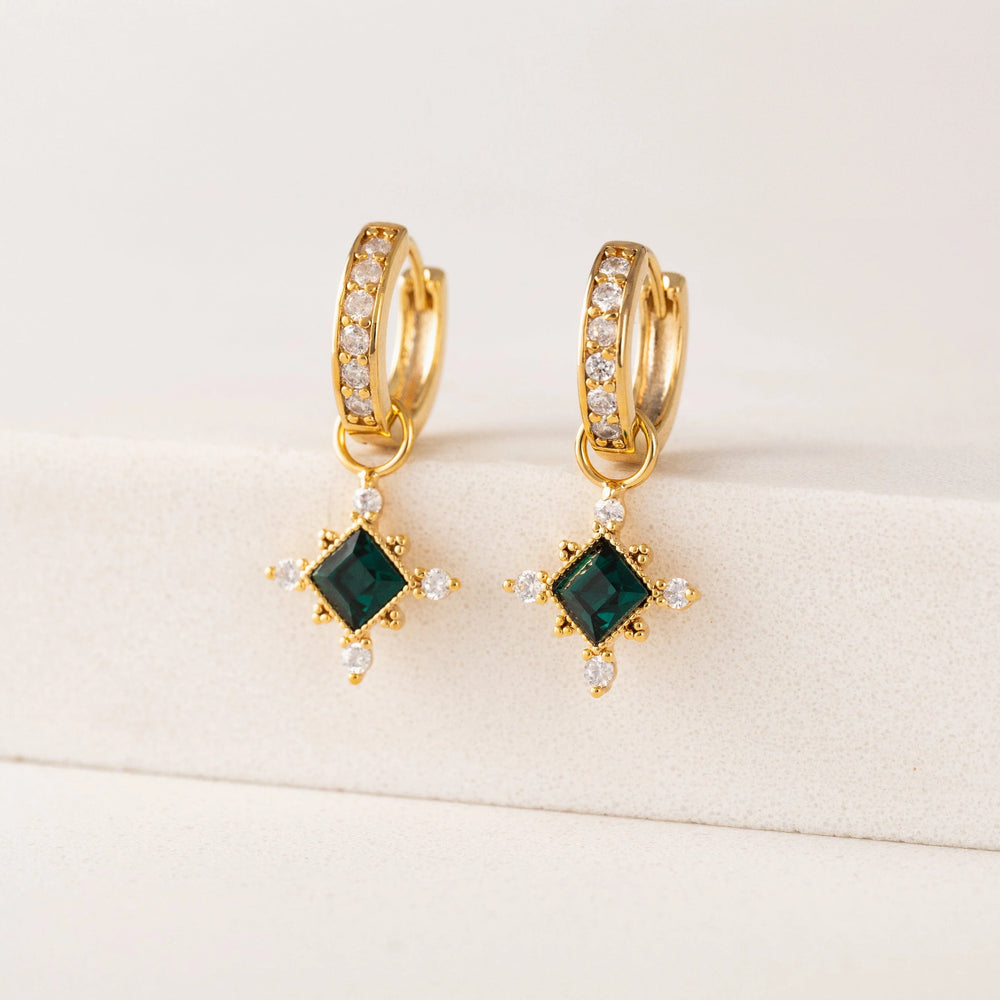Gold hoop earrings with green gemstones on a beige background