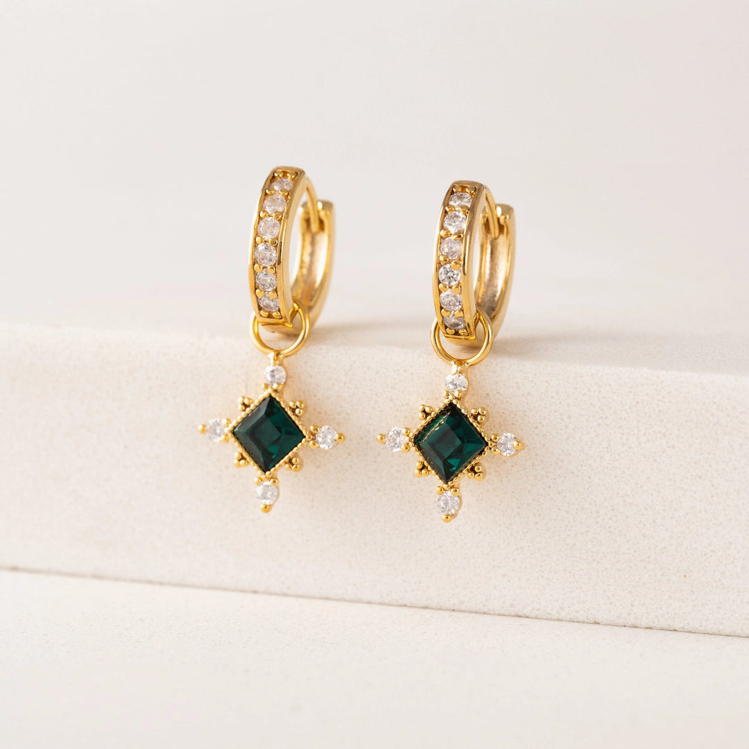 Gold hoop earrings with green gemstones on a beige background