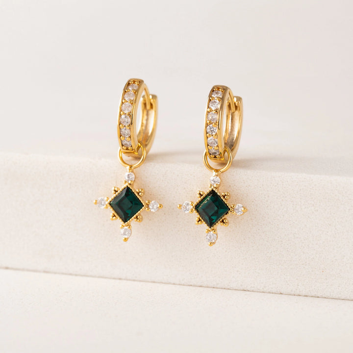 Gold hoop earrings with green gemstones on a beige background