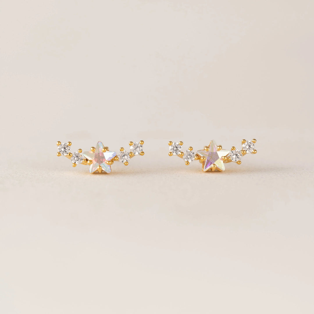 Pair of gold and silver star-shaped earrings on a beige background