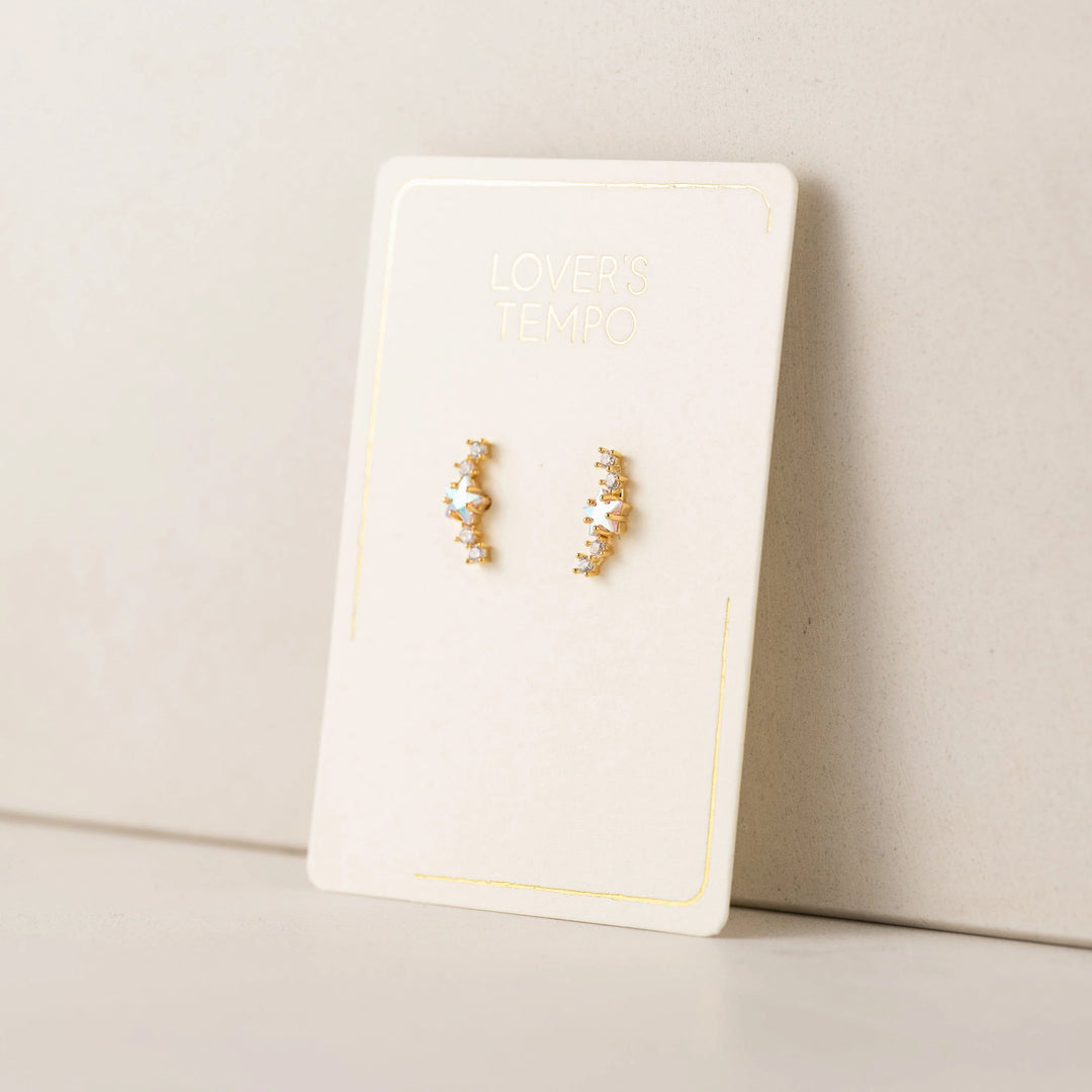 Gold star climber earrings on a white card with a beige background