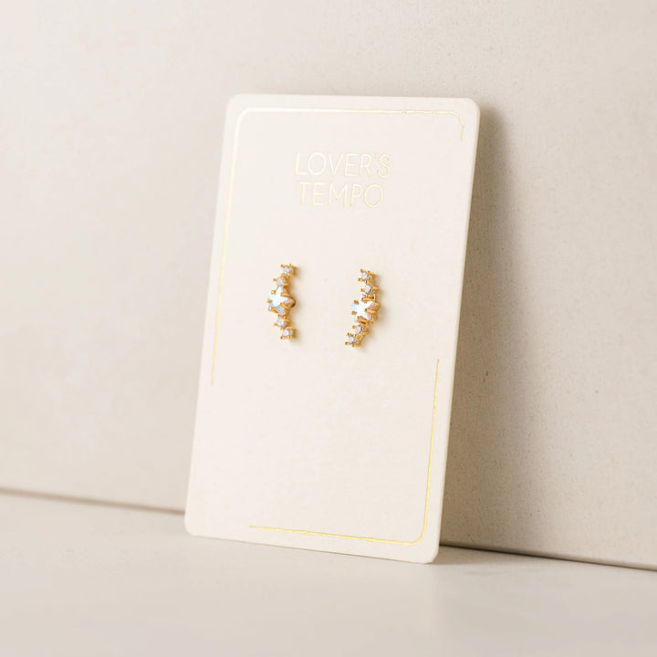 Gold star climber earrings on a white card with a beige background
