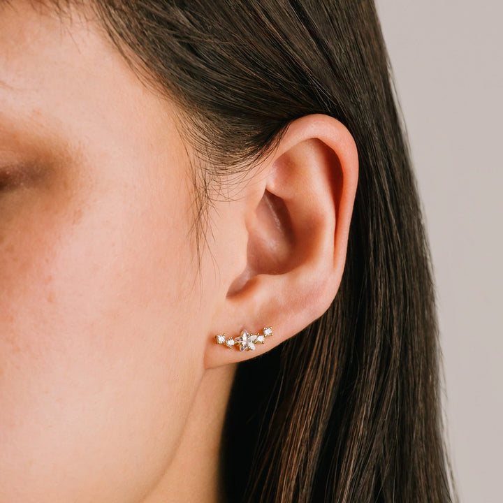 Close-up of an ear wearing a star climber earring with a neutral background