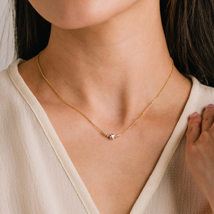 Gold necklace with a small pendant on a person wearing a beige top.