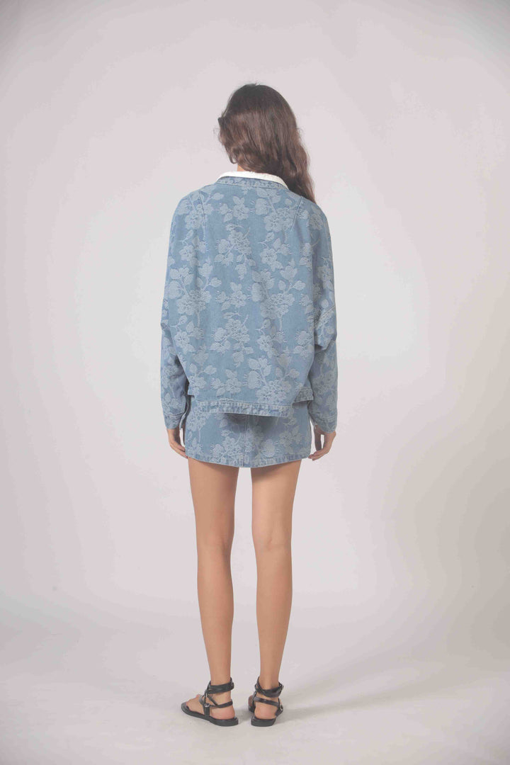 Embroidered denim jacket by The Korner with colorful floral embroidery, classic button-up front, and relaxed fit.