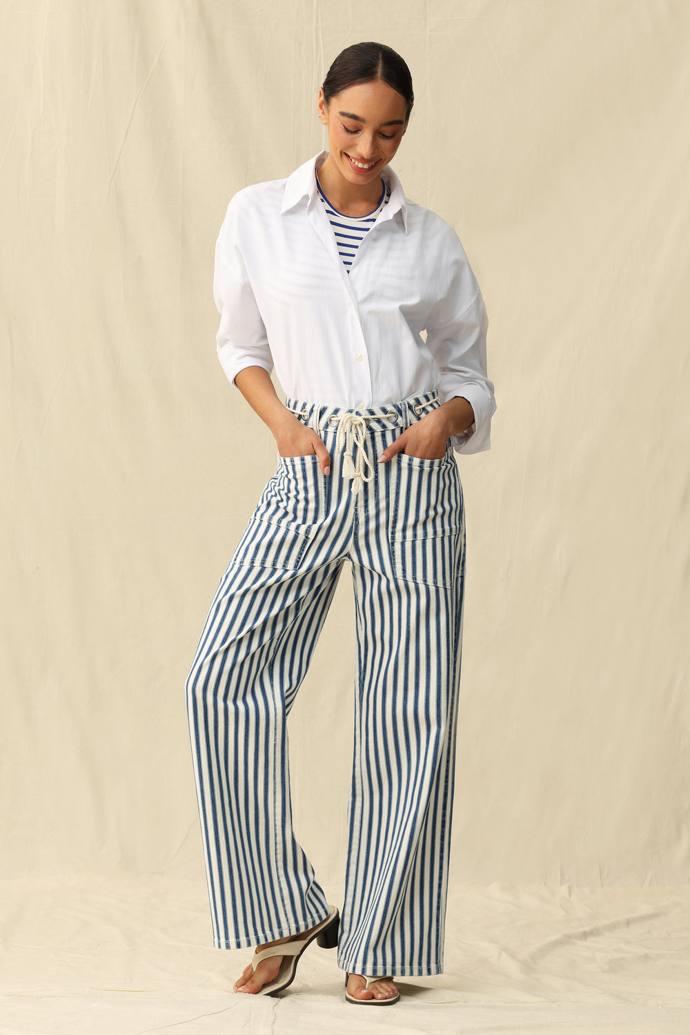 Woman wearing a white shirt and striped pants against a beige background