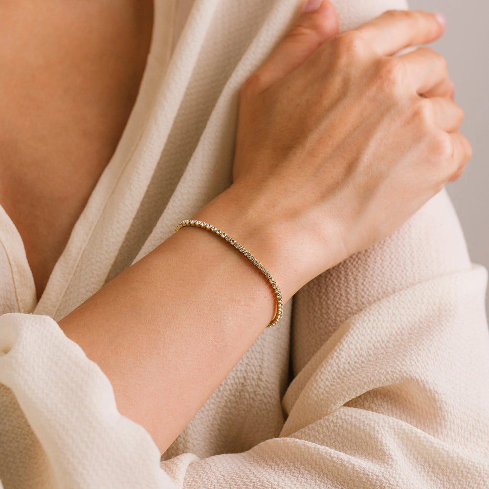 Close-up of a hand wearing a gold bracelet with a neutral background