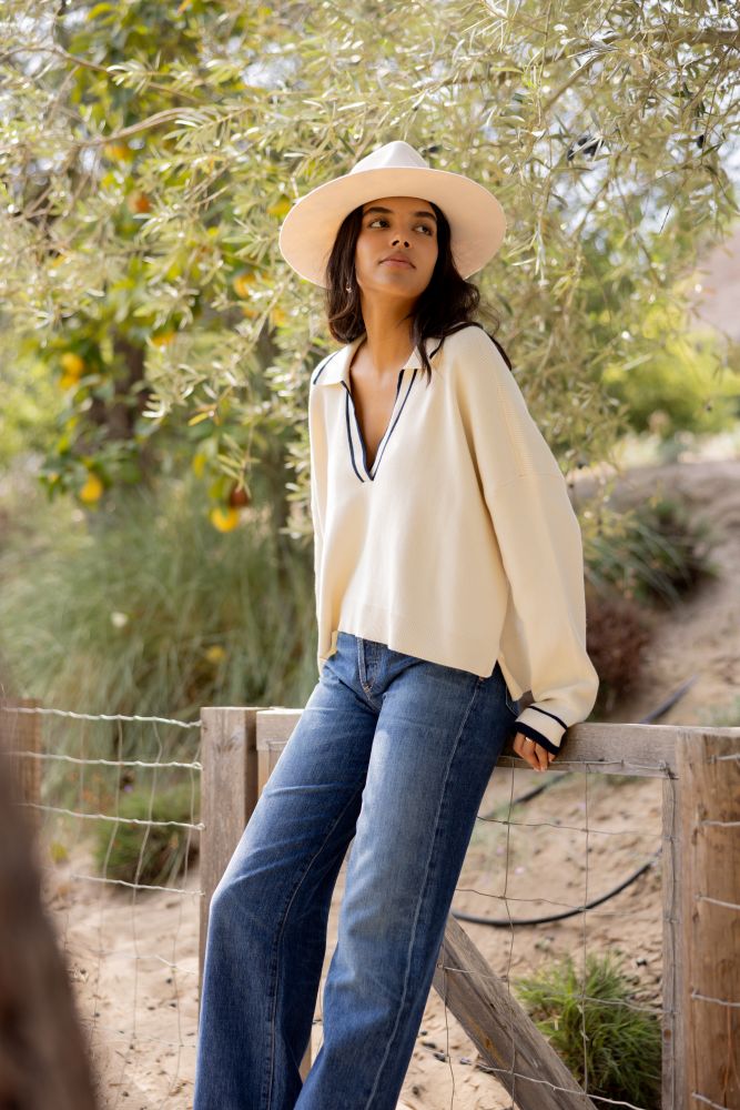 Woman wearing a beige hat and white sweater with blue jeans, standing outdoors.