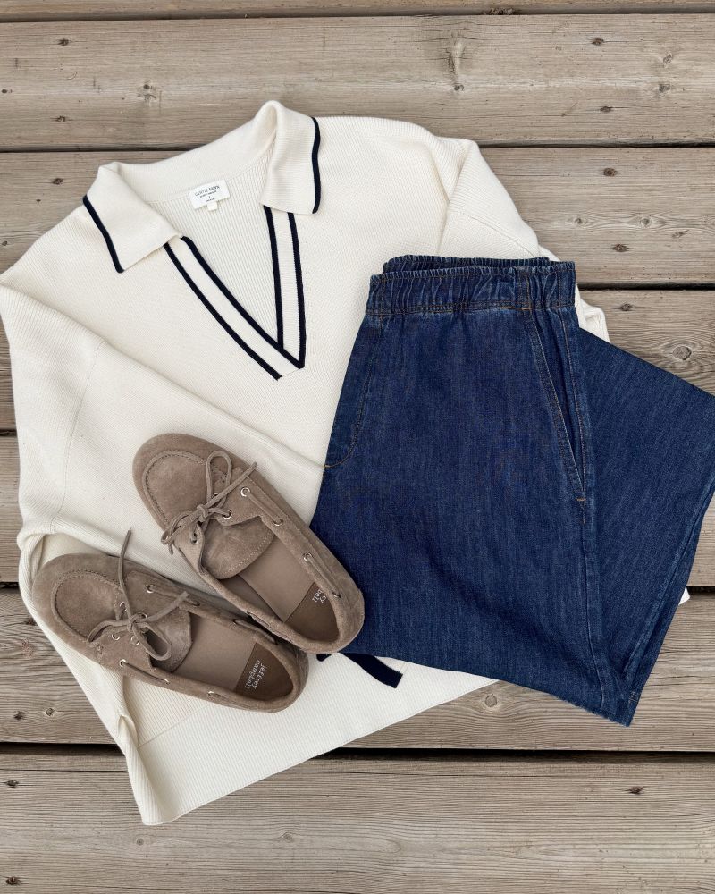 White sweater with black trim, blue jeans, and brown shoes on a wooden surface