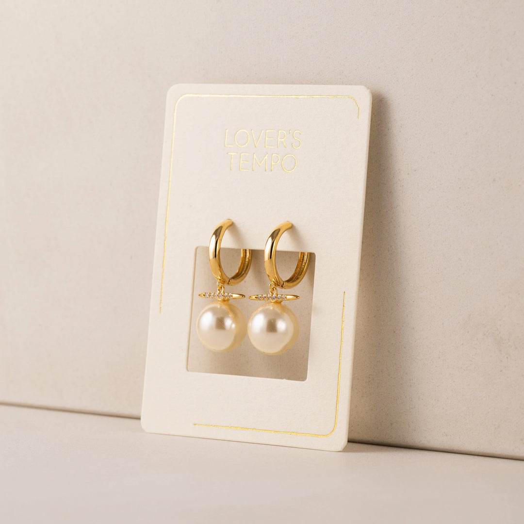 Gold hoop earrings with pearl drops on a branded card against a beige background