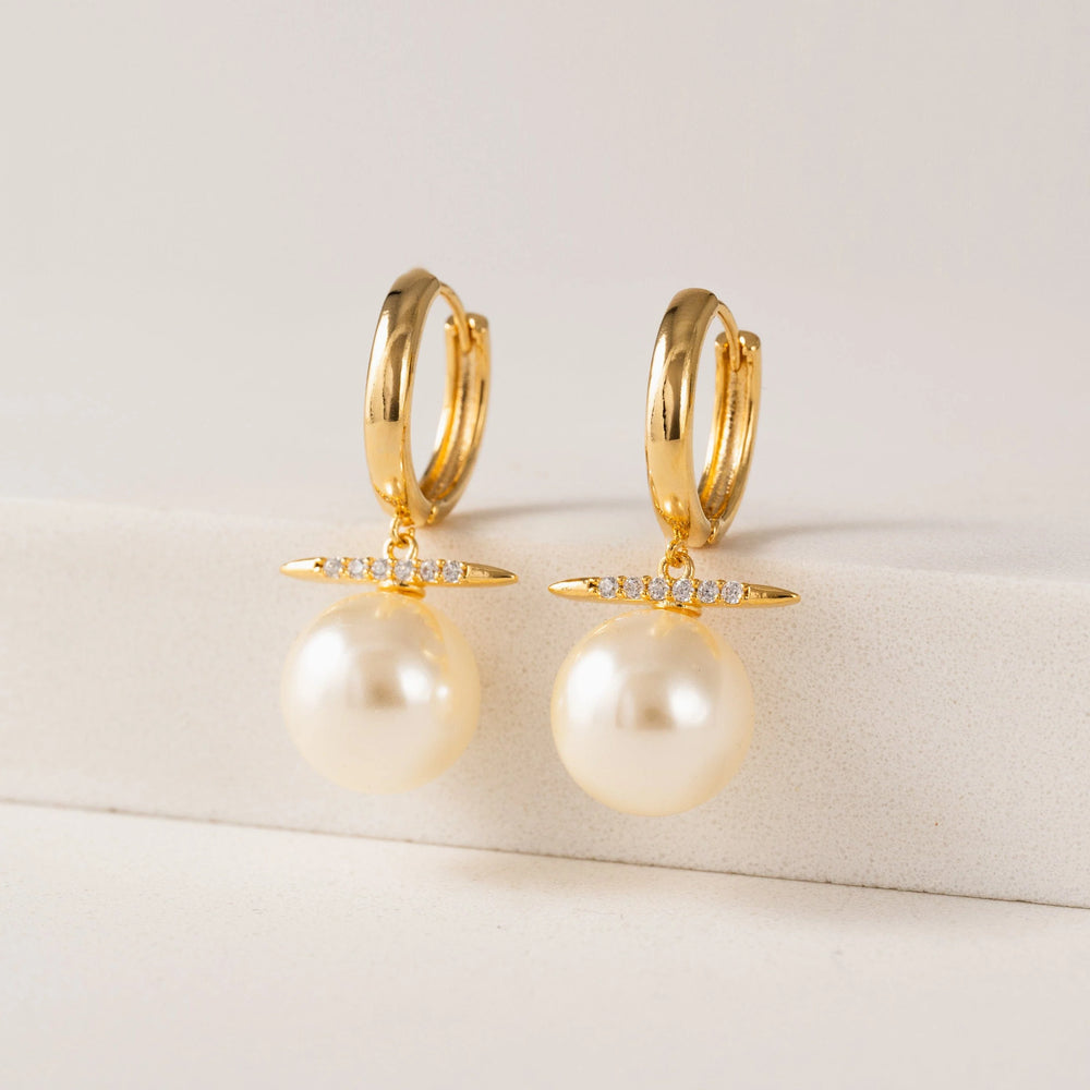 Gold hoop earrings with pearl drops on a light background