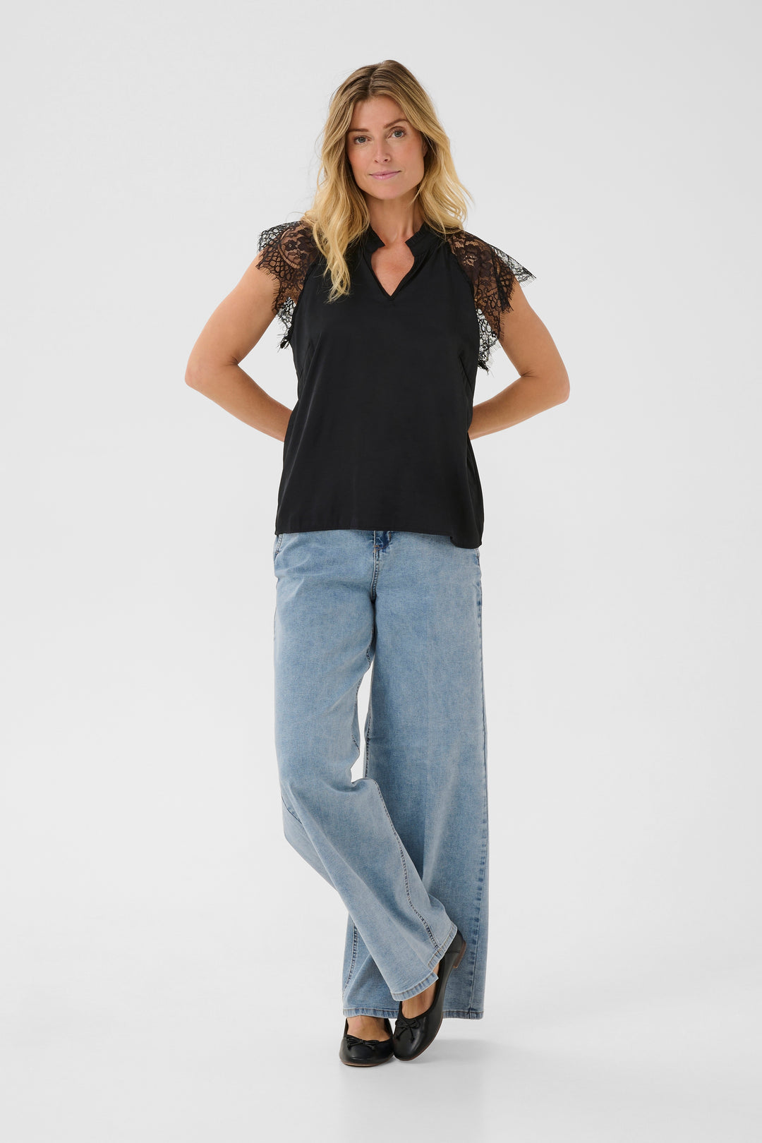 Woman wearing a black top with lace sleeves and light blue jeans on a white background