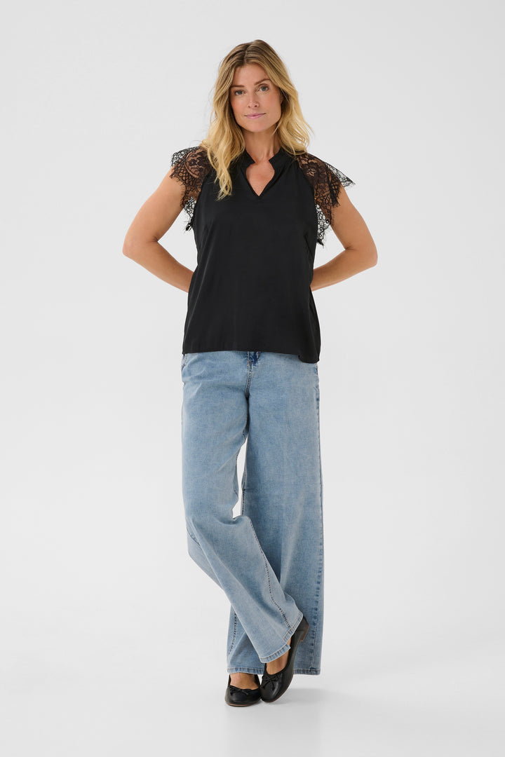 Woman wearing a black top with lace sleeves and light blue jeans on a white background
