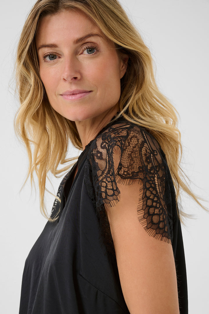 Woman wearing a black top with lace sleeves against a white background