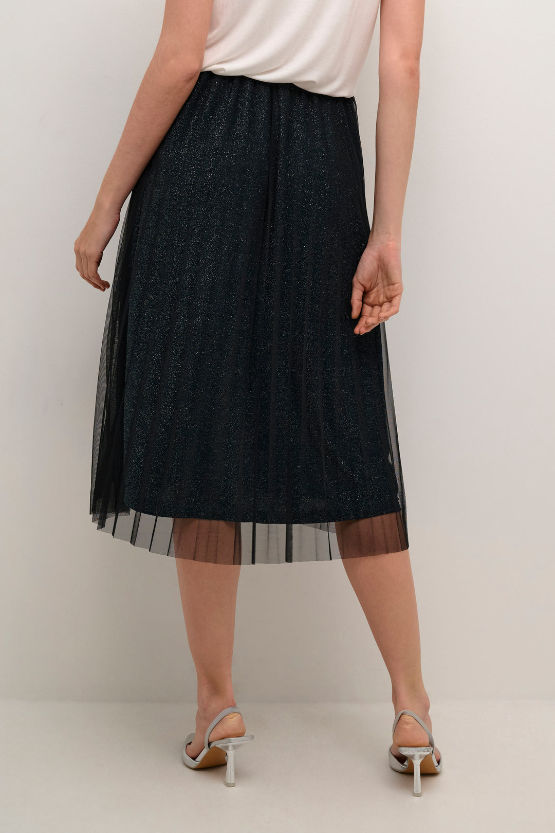 Person wearing a black sheer skirt over a white top on a plain background