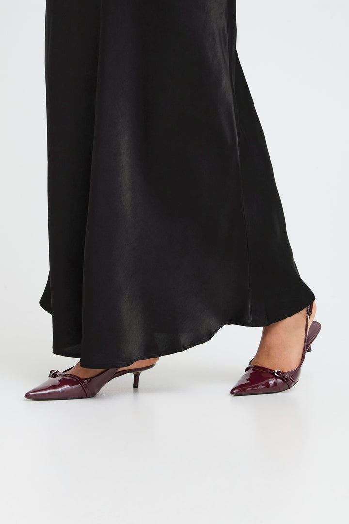 Person wearing black skirt and burgundy shoes on a white background