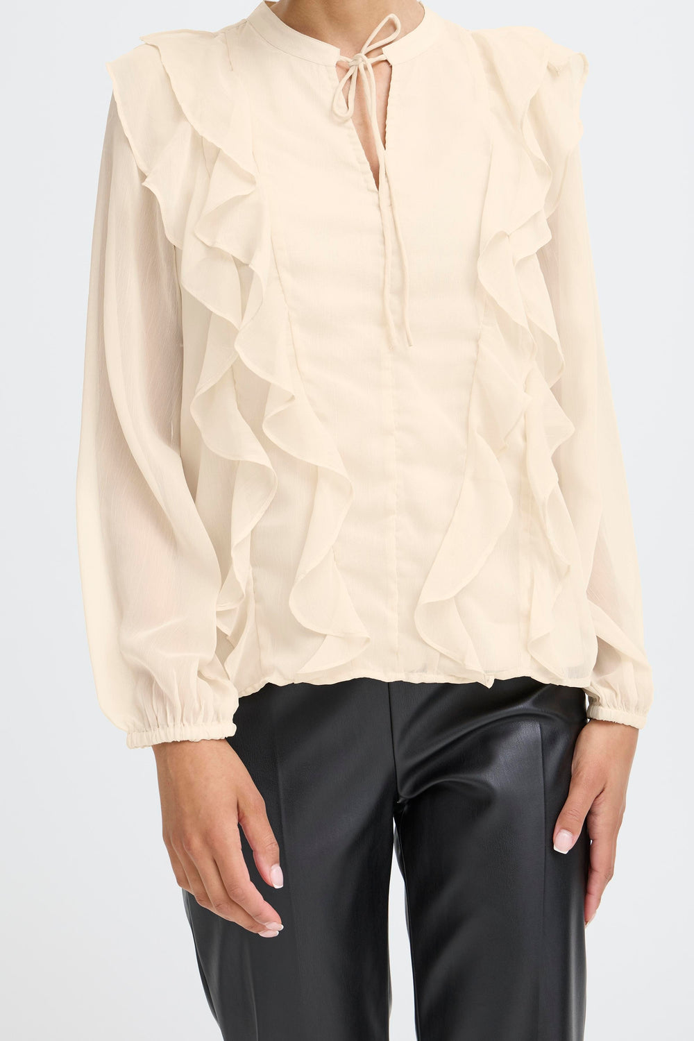 Beige blouse with ruffled sleeves and black pants on a white background