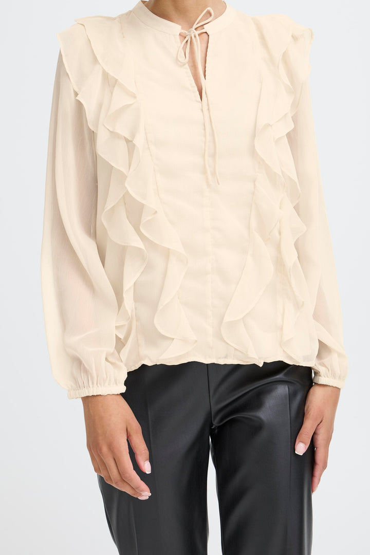 Beige blouse with ruffled sleeves and black pants on a white background