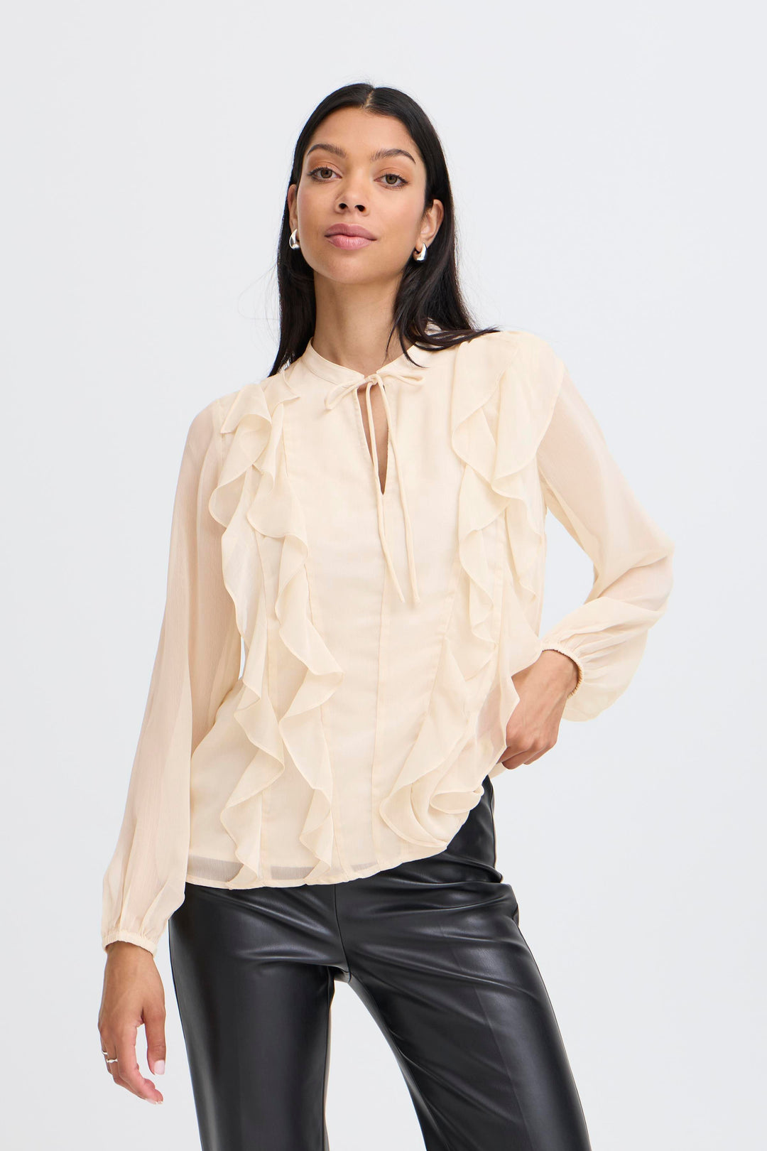 Woman wearing a beige blouse with ruffled details and black pants on a white background