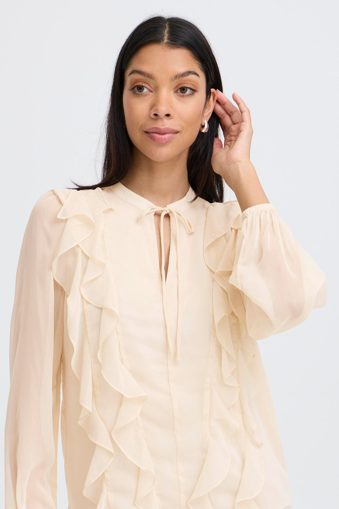 Woman wearing a beige blouse with ruffled sleeves on a white background