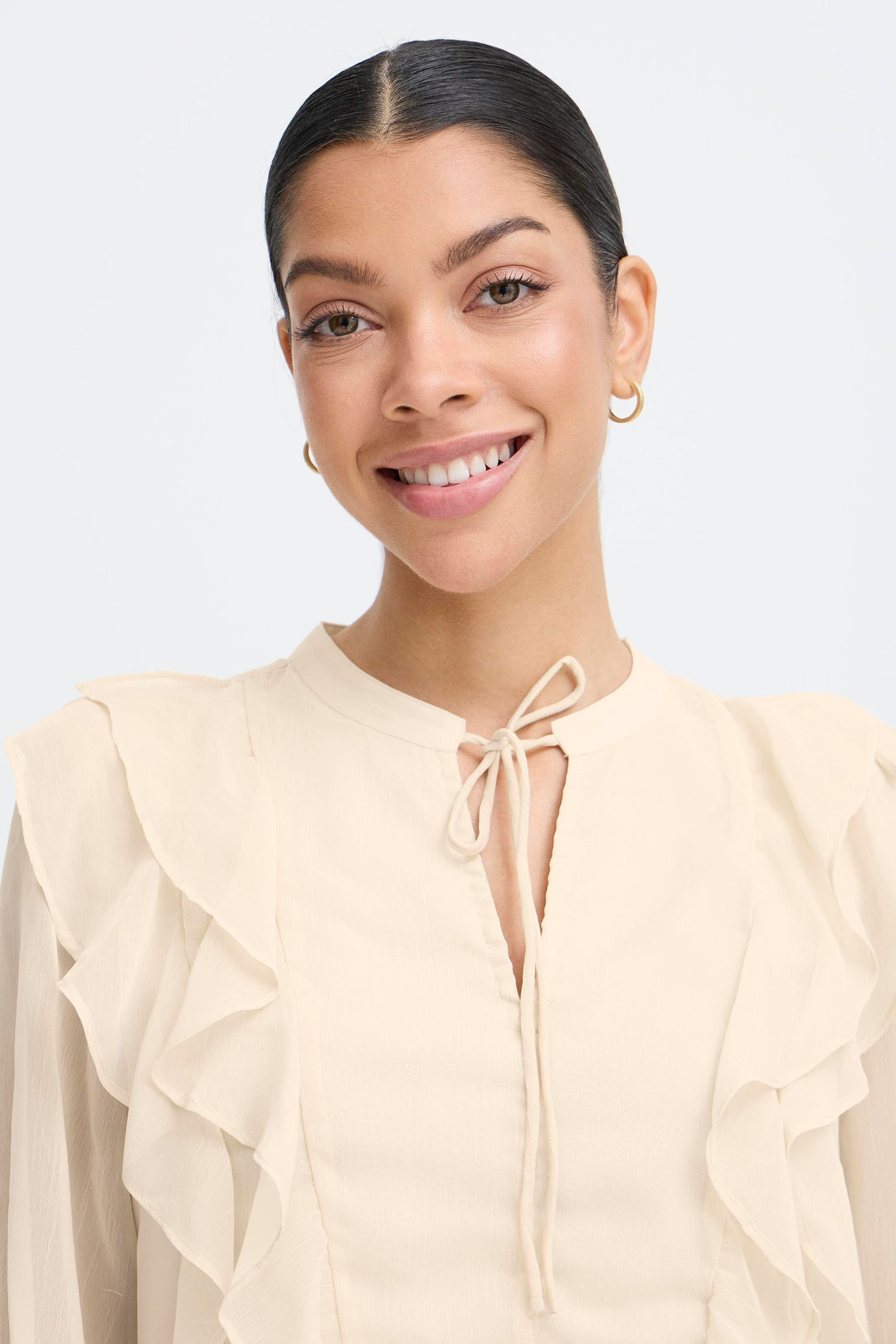 Woman wearing a beige blouse with ruffled sleeves on a light gray background