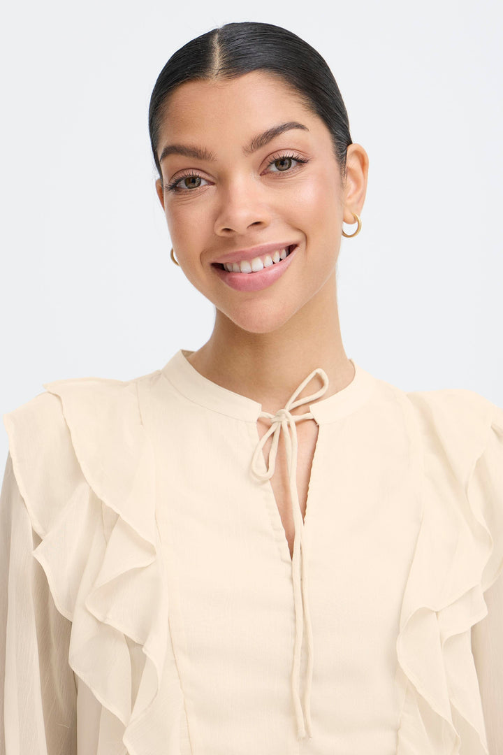 Woman wearing a beige blouse with ruffled sleeves on a light gray background