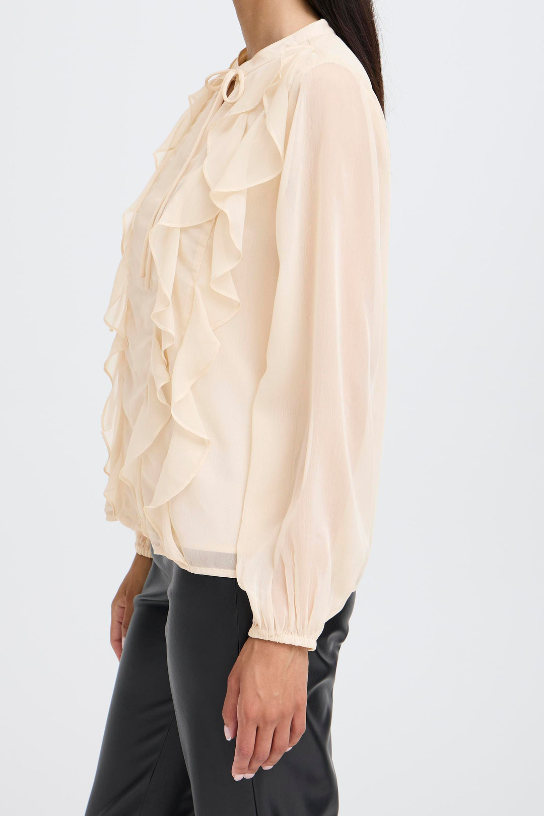 Beige blouse with ruffled details worn by a person on a white background