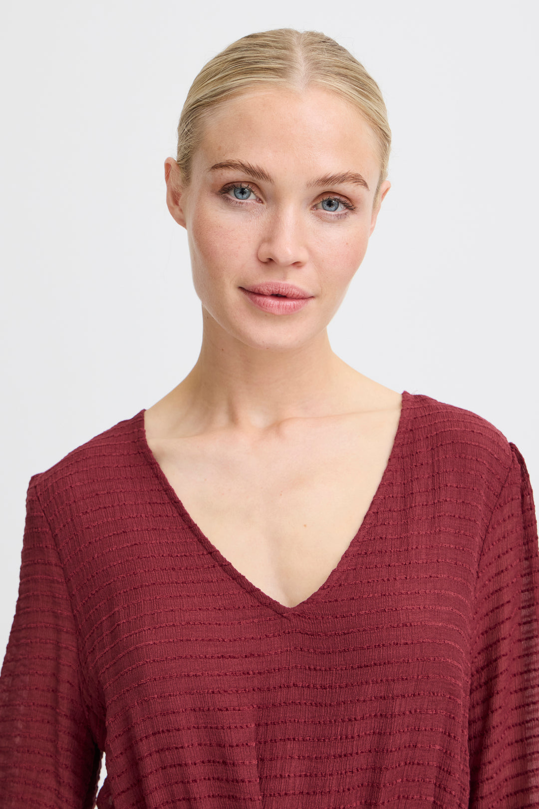 Woman wearing a burgundy textured top against a plain background