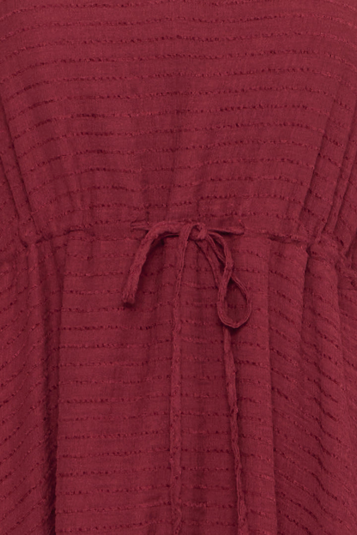 Close-up of a textured burgundy dress with a drawstring waist.