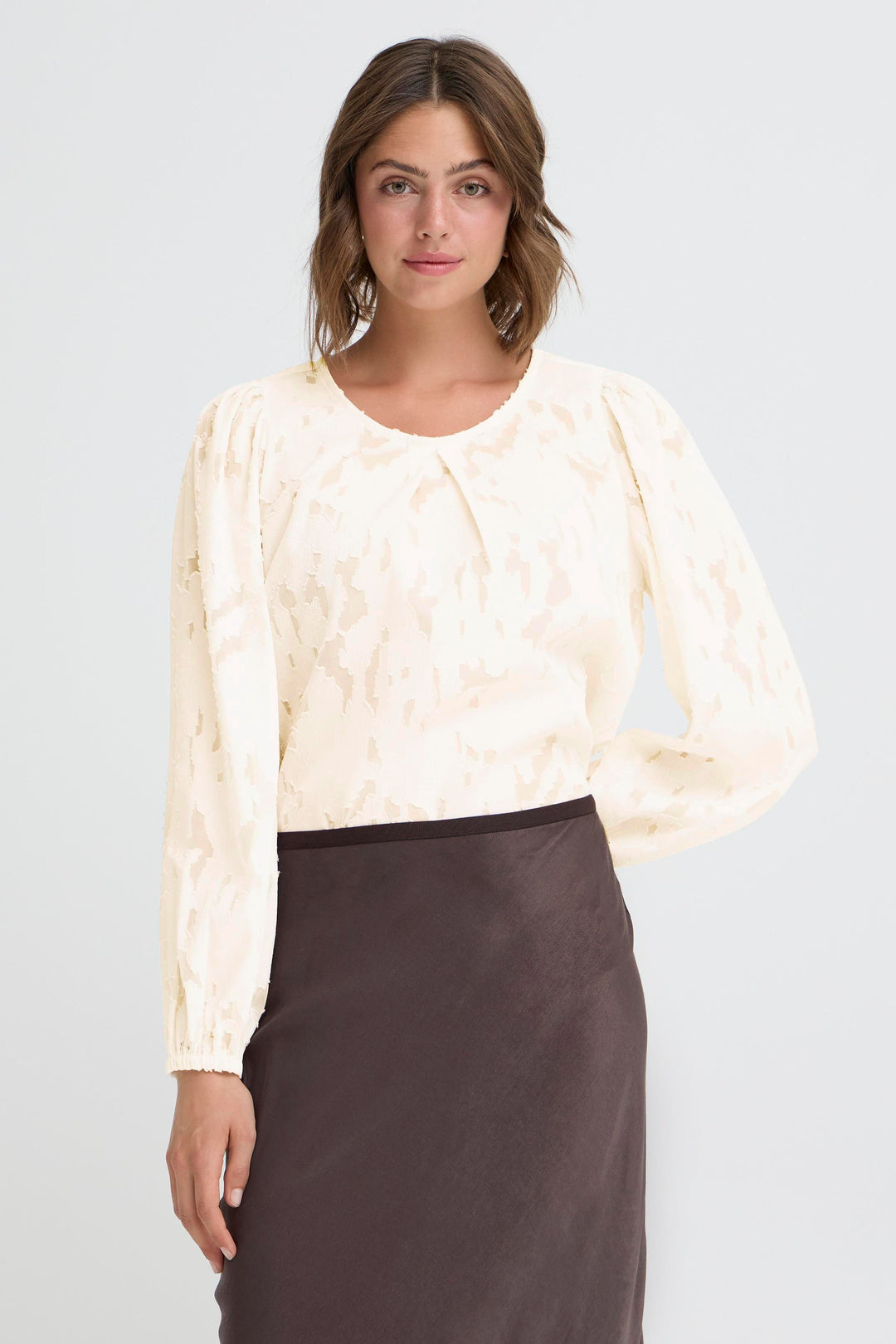 Woman wearing a cream blouse with long sleeves and a dark skirt on a light gray background